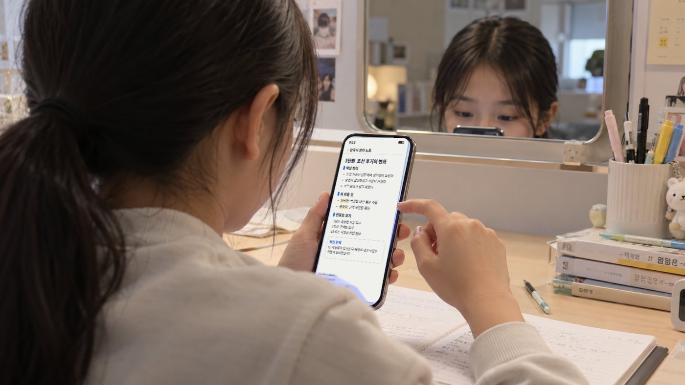 책상에서 휴대폰으로 공부 자료를 넘기는 학생